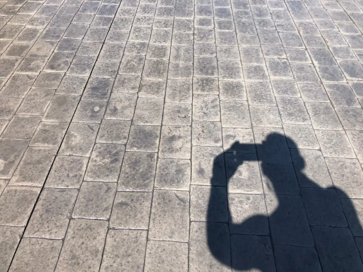 A person is standing on the sidewalk with their shadow